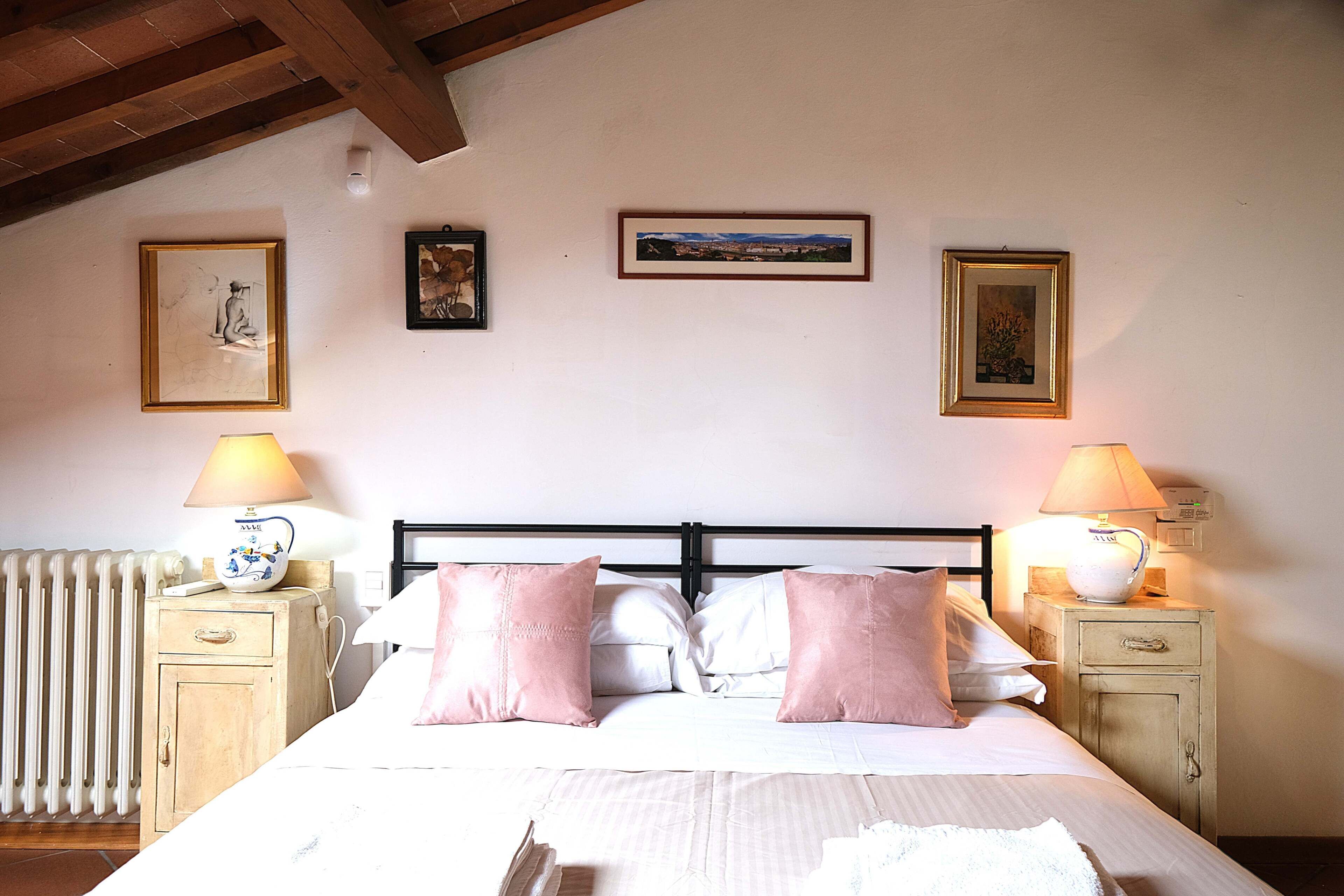 A bedroom with a bed, two bedside tables, a radiator, and wall-mounted artwork.