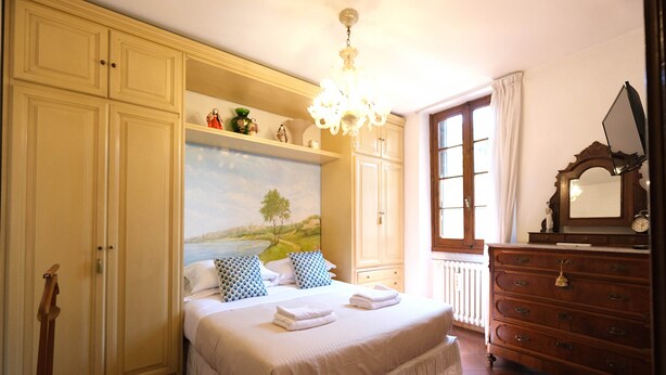 A bedroom with a bed, a dresser, a painting, and a chandelier. - Wine Apartments Florence Soave (Firenze)