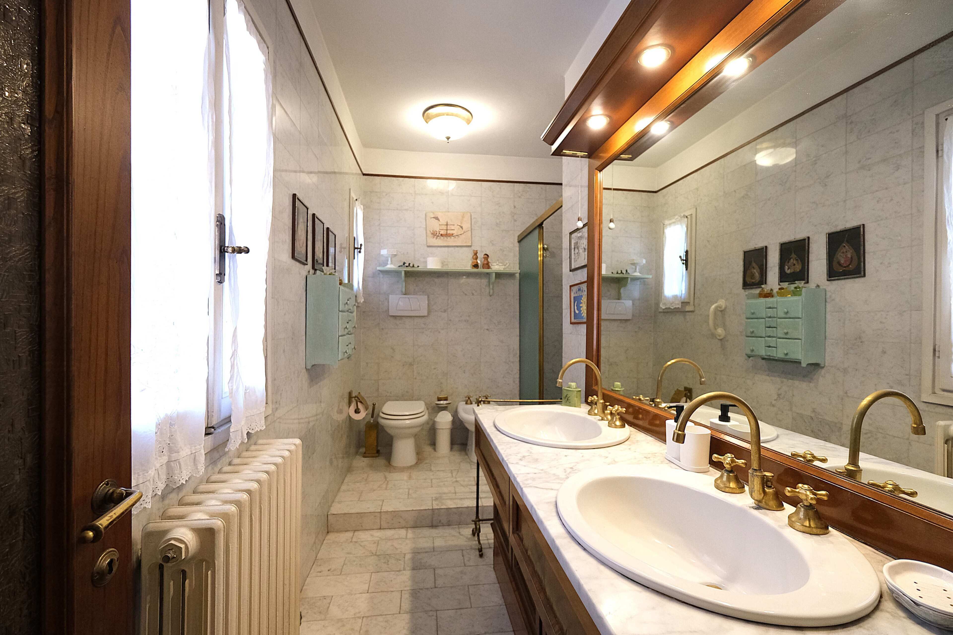 Ein Badezimmer mit zwei Waschbecken, einer Toilette, einem Heizkörper und einem Spiegel.