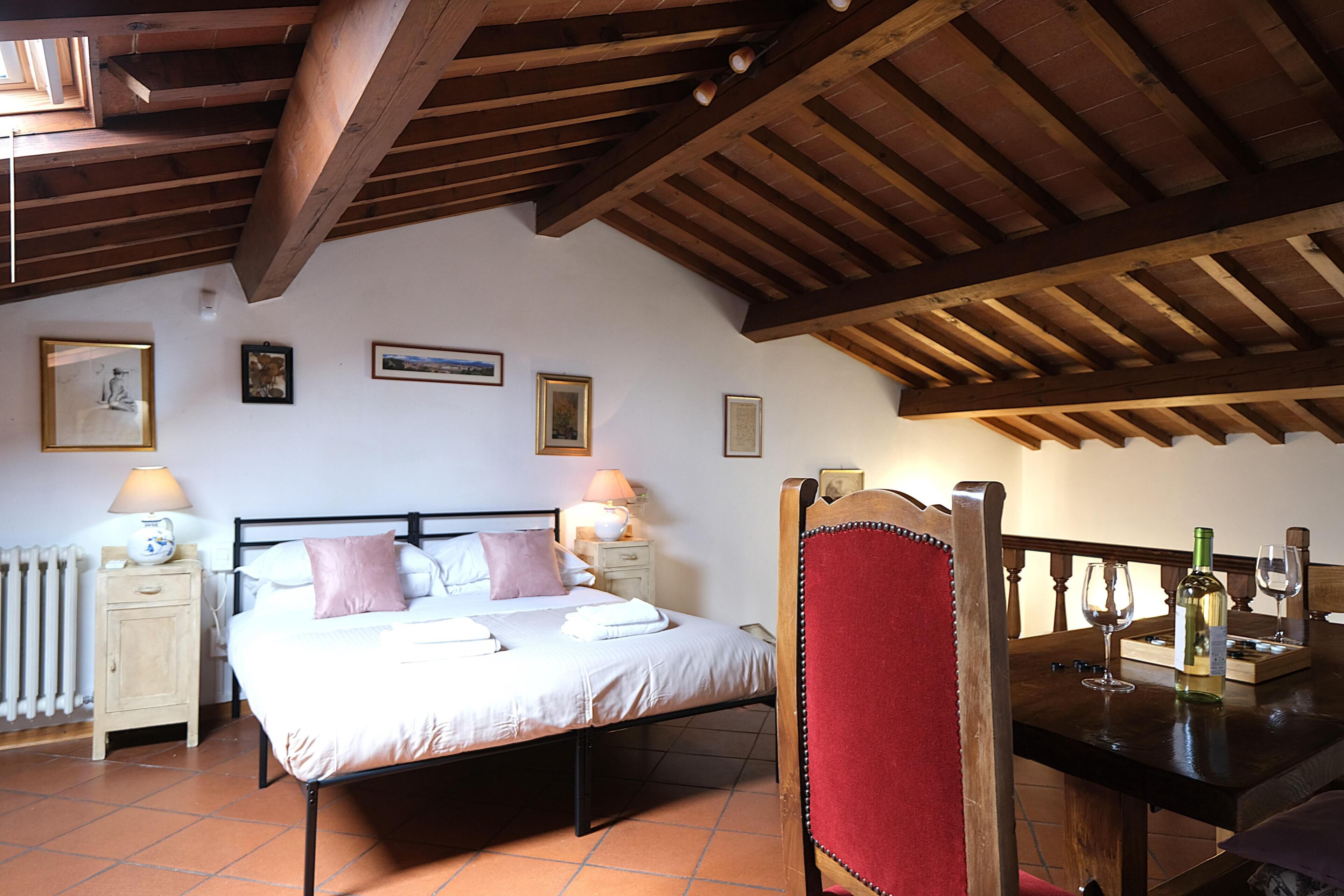 Ein Schlafzimmer mit einem Bett, Nachttischen, einem Sessel und einem Esstisch mit Weinflaschen.
