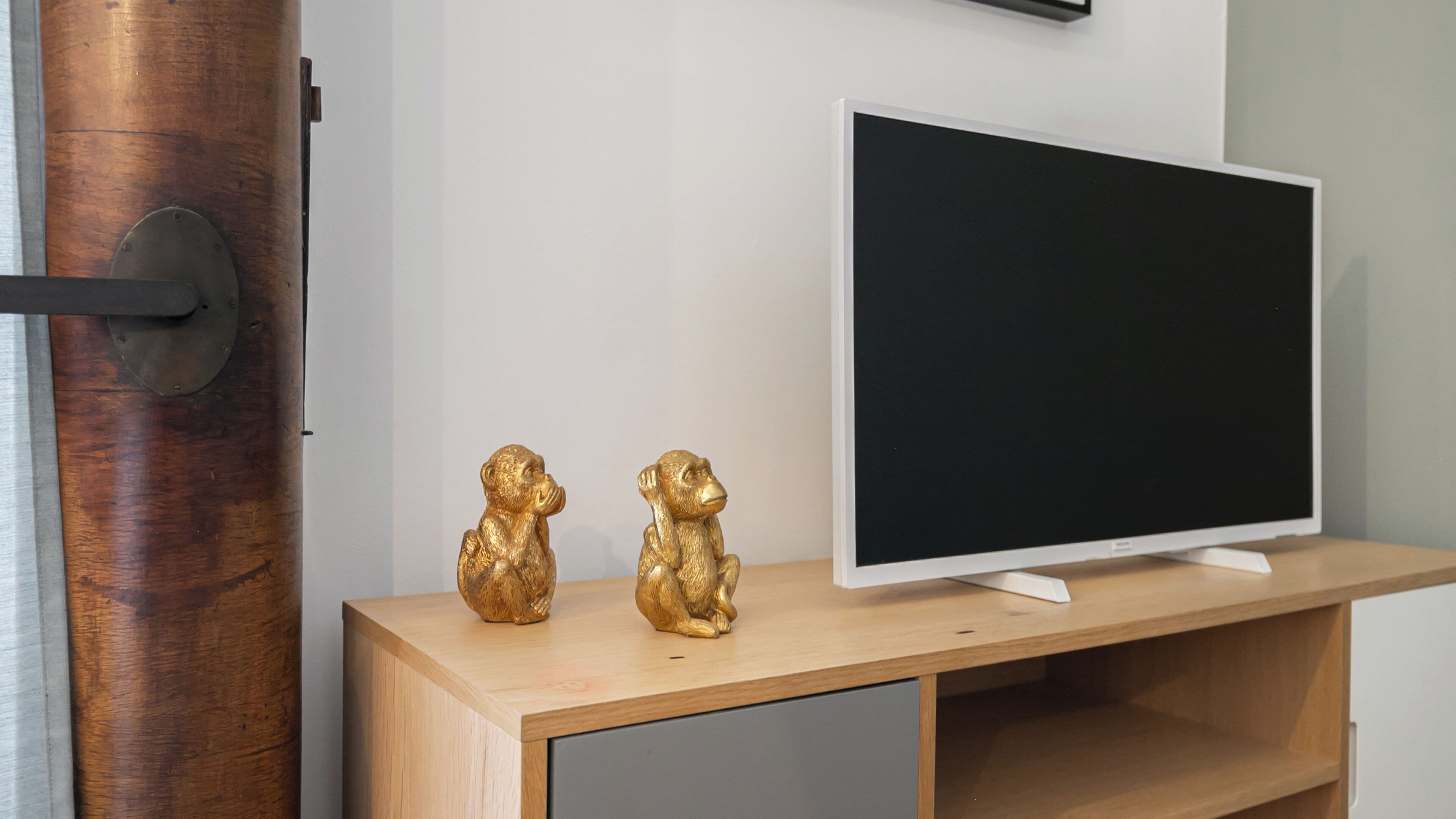Un meuble en bois pour la télévision, sur lequel est posée une télévision à écran plat, ainsi que deux statuettes de singes dorées et une porte dotée d’une poignée métallique.