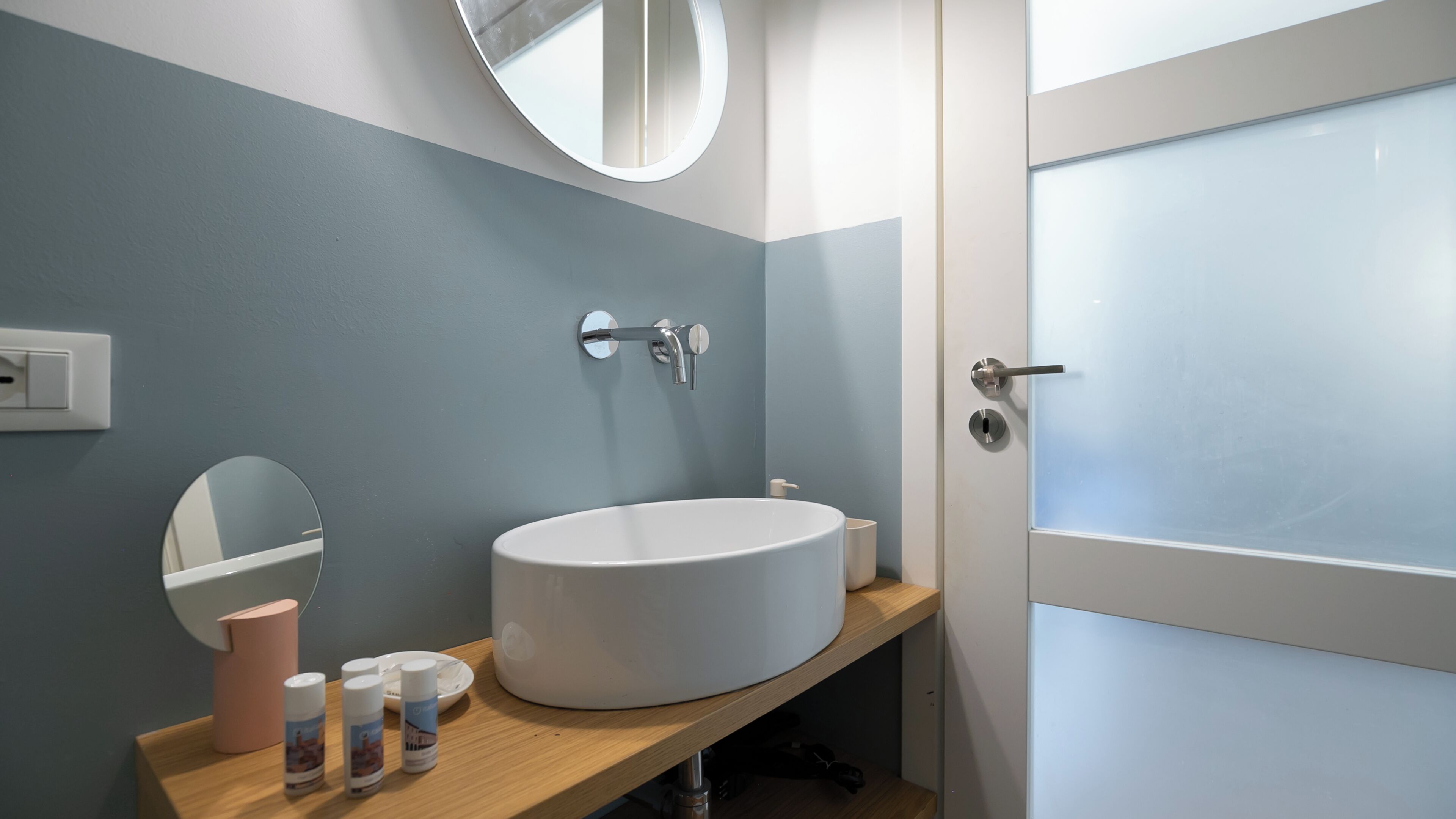 A bathroom with a round white sink, a mirror, a toilet, and a door with frosted glass panels.