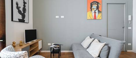 Una sala de estar moderna con un sofá gris, un televisor sobre un mueble de madera, una mesita con revistas y obras de arte en la pared.