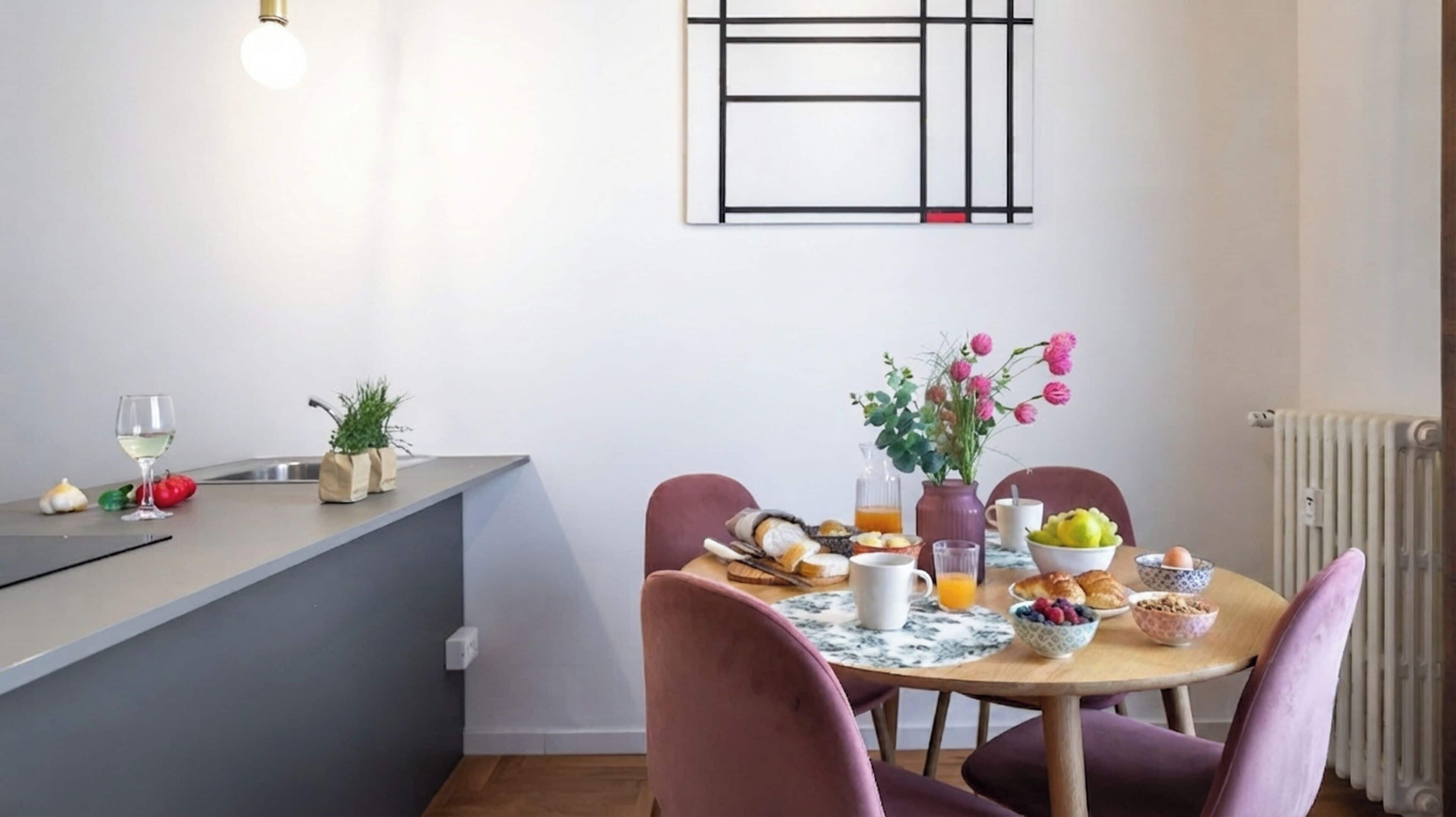 A modern kitchen with a dining area, featuring a marble countertop, a built-in sink, and a dining table with chairs.