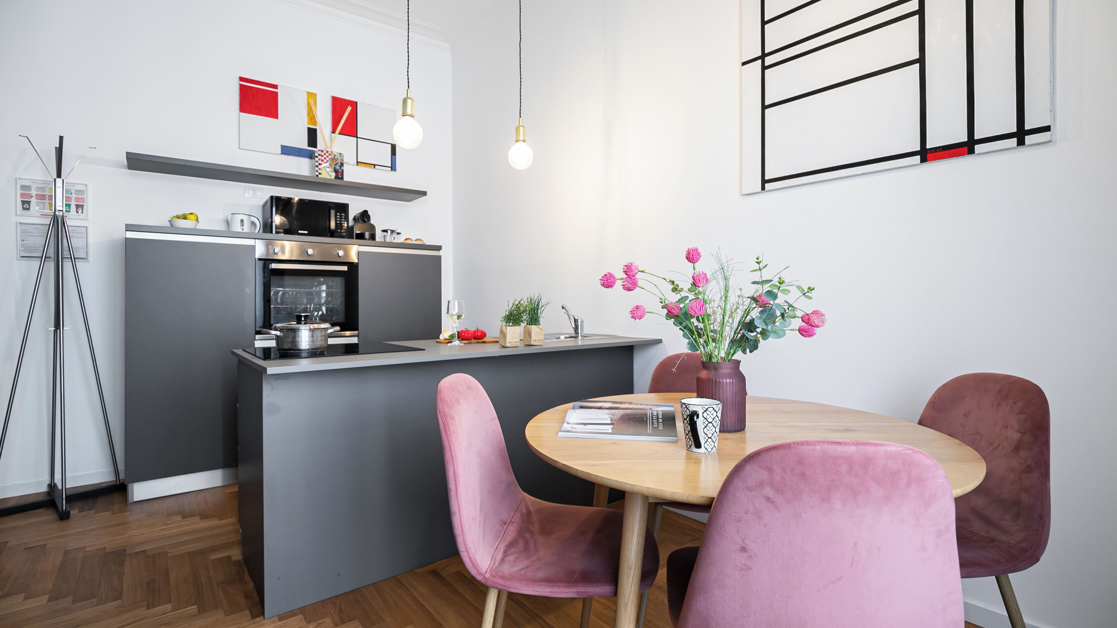 Une cuisine moderne avec un îlot central, un coin repas avec des chaises roses et un vase rempli de fleurs sur la table.
