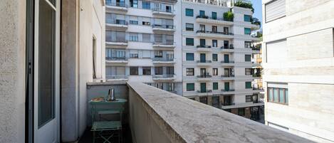 A balcony with a metal chair, a small table, and a metal drying rack.