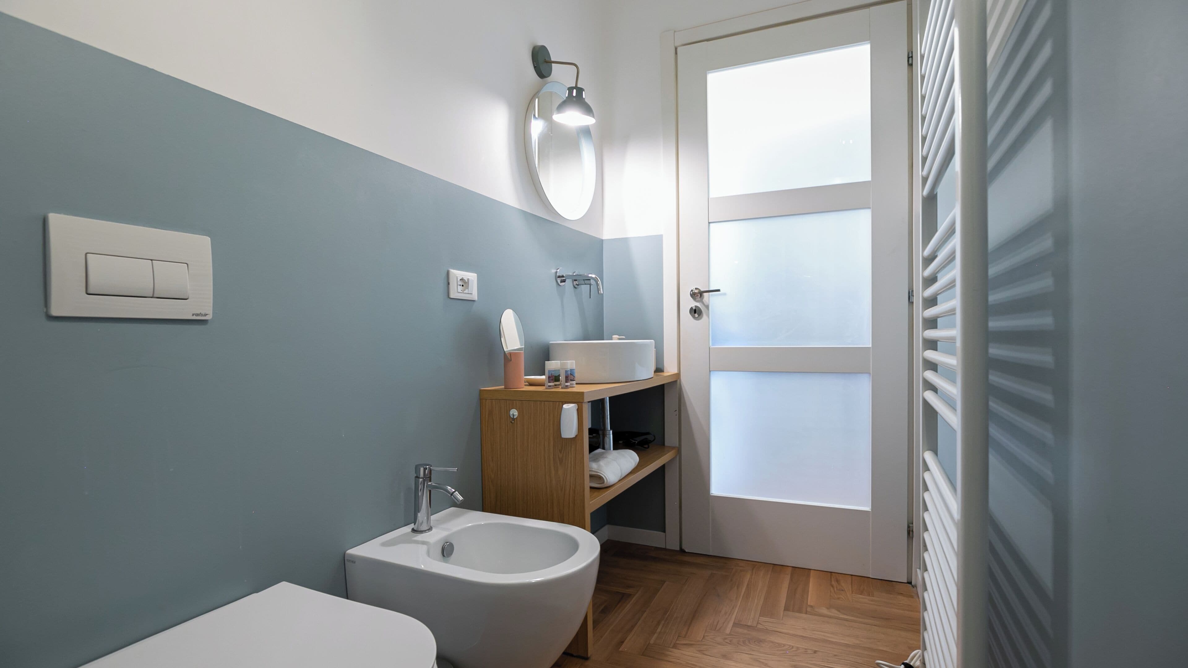 Une petite salle de bain équipée d’un bidet, d’un lavabo, d’un miroir et d’un porte-serviettes.