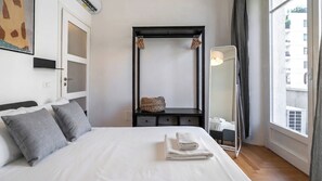 Habitación de hotel con cama, mesita de noche con lámpara, un espejo grande y vistas al exterior.