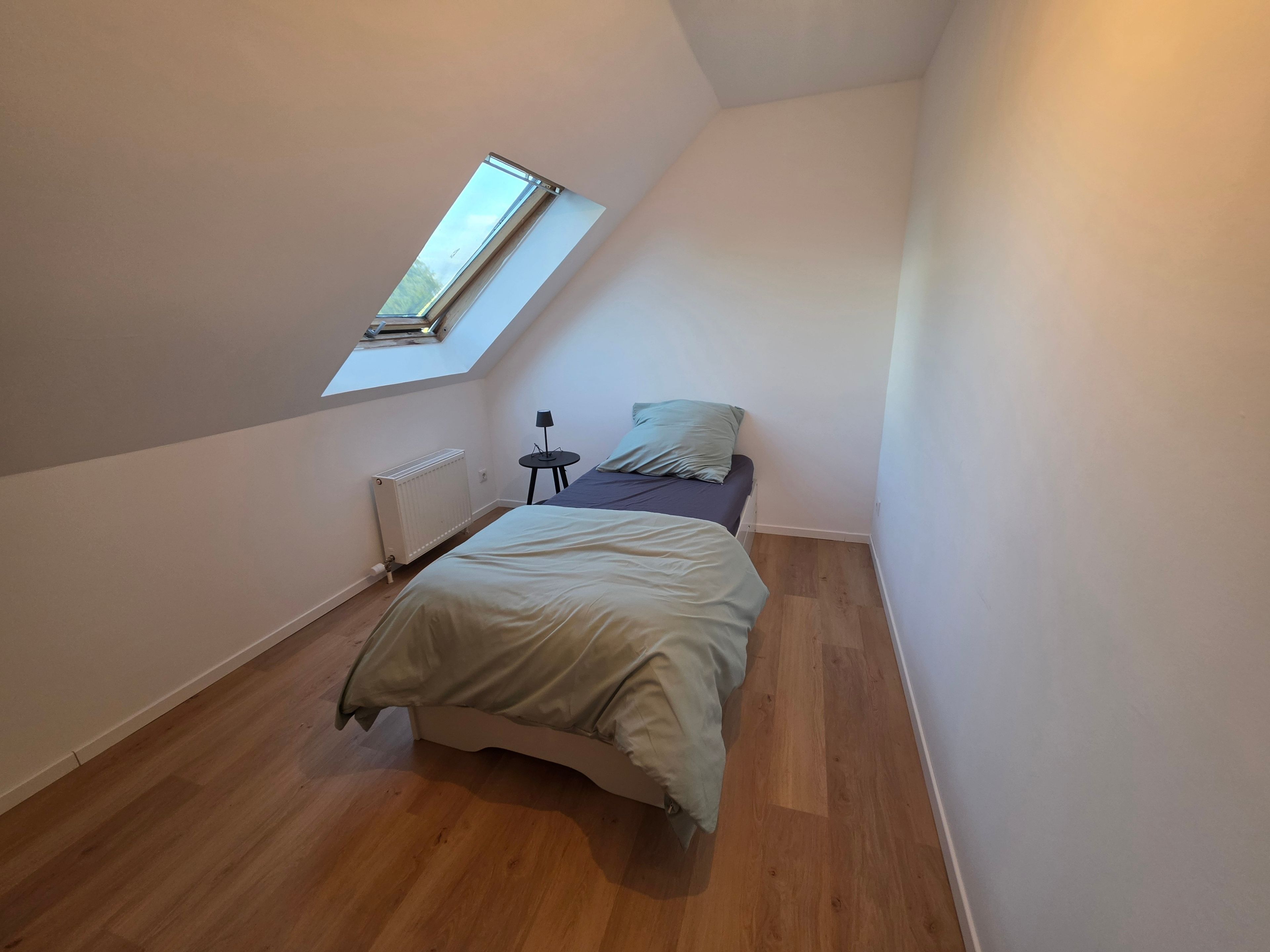 A small, sloped room with a bed, a small table, and a radiator.