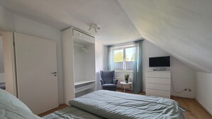 Een slaapkamer met een bed, een stoel, een televisie en een kledingkast.