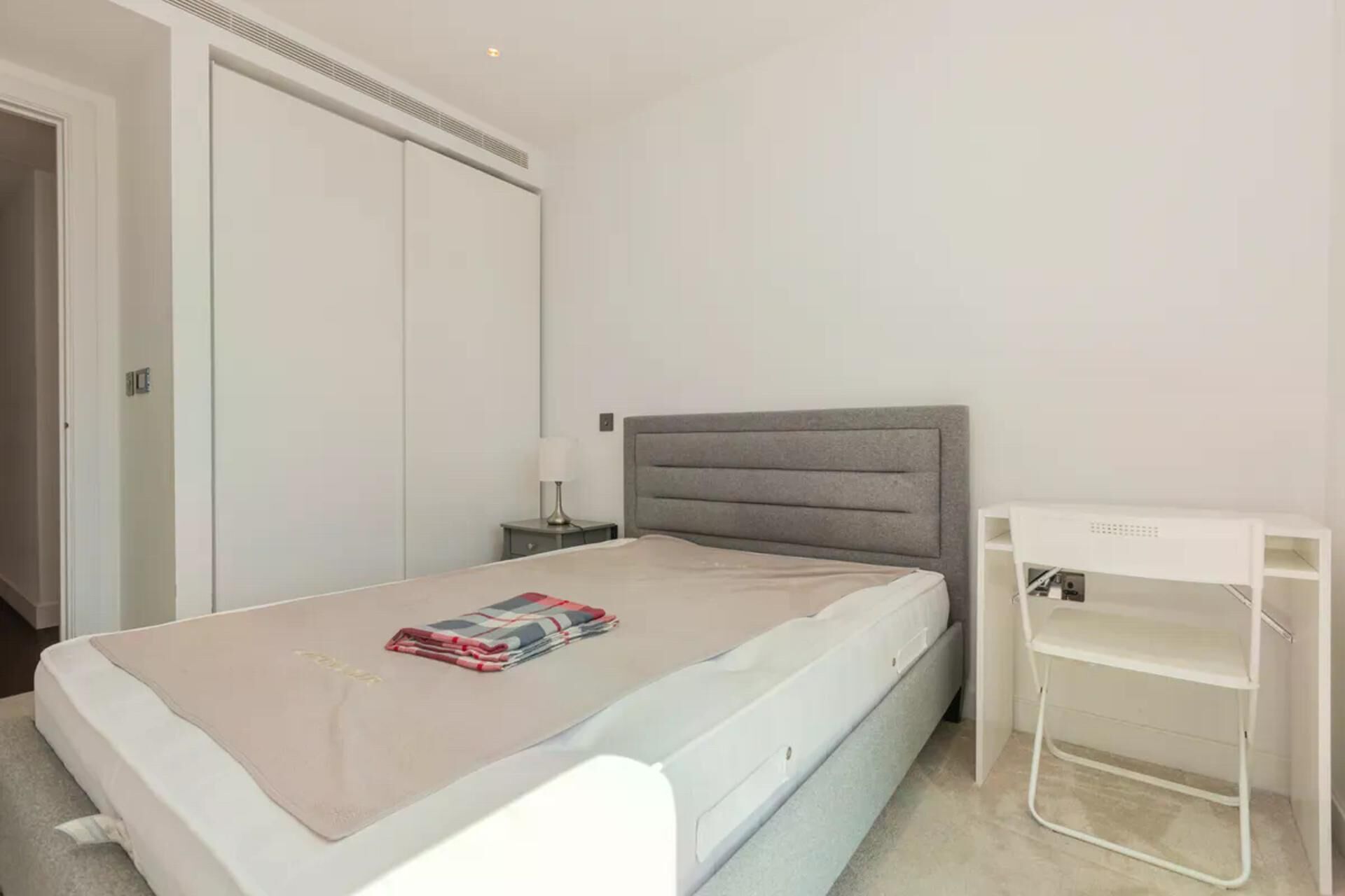 Ein Schlafzimmer mit einem Bett, einem Nachttisch, einer Lampe, einem Kleiderschrank und einem Schreibtisch.