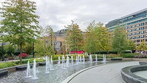 Una fuente pública con chorros de agua, rodeada de árboles y edificios modernos.