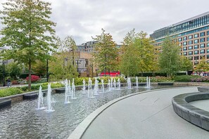 Ein öffentlicher Brunnen mit Wasserspielen, umgeben von Bäumen und modernen Gebäuden.