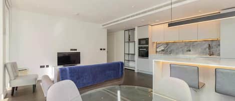 Una sala de estar moderna con una mesa de centro de vidrio, un televisor de pantalla plana y un sofá azul.