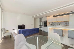 En moderne stue med et sofabord i glas, et fladskærms-TV og en blå sofa.