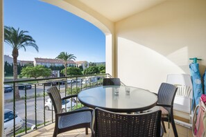 Ein Balkon mit rundem Tisch und Stühlen, Blick auf eine Straße mit Autos, und ein Gebäude mit rotem Dach im Hintergrund.