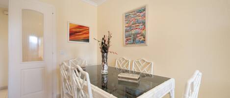 Un comedor con una mesa de vidrio, sillas blancas y dos obras de arte enmarcadas en la pared.