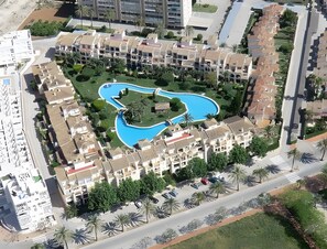 Ein Resort mit einem zentralen Schwimmbad, mehreren Gebäuden und Palmen.