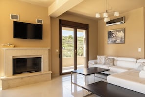 A modern living room with a fireplace, a flat-screen TV, a sofa, and a dining table. - Villa Mononaftis (Heraklion)