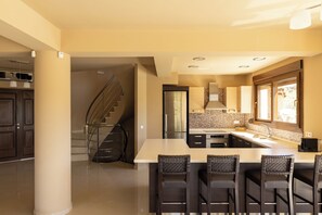 A modern kitchen with a central island, bar stools, and a staircase leading to another level. - Villa Mononaftis (Heraklion)