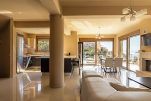 A modern kitchen with a central island, a dining area with a view, and a living room with a sofa. - Villa Mononaftis (Heraklion)