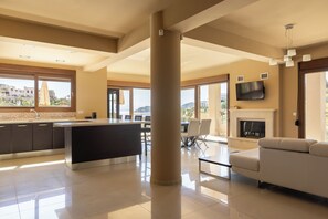 A spacious living area with a large central column, a kitchen with a view, a dining area with a table and chairs, and a fireplace. - Villa Mononaftis (Heraklion)