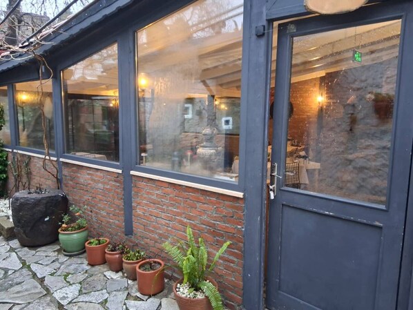 A building with a glass facade, a brick wall, and a door. There are potted plants outside.