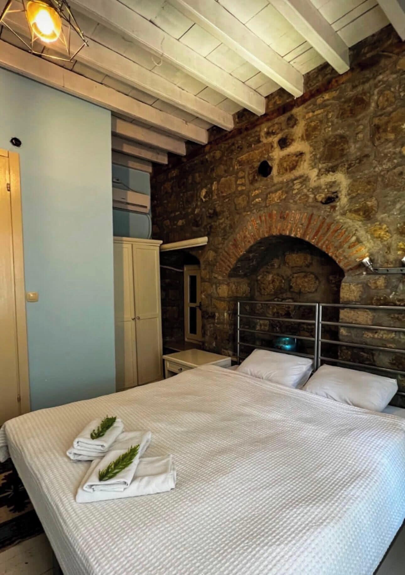 A bed with white linens and towels, a stone wall, and a metal headboard.