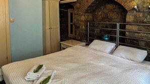 A bed with white linens and towels, a stone wall, and a metal headboard. - ADATEPE OTEL KAZDAĞLARI (Ayvacik)