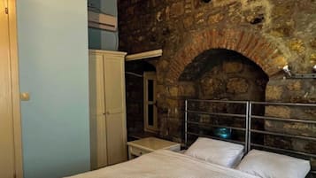 A bed with white linens and towels, a stone wall, and a metal headboard.