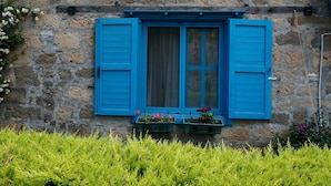 A stone building with a window featuring blue shutters and a curtain. - ADATEPE OTEL KAZDAĞLARI (Ayvacik)