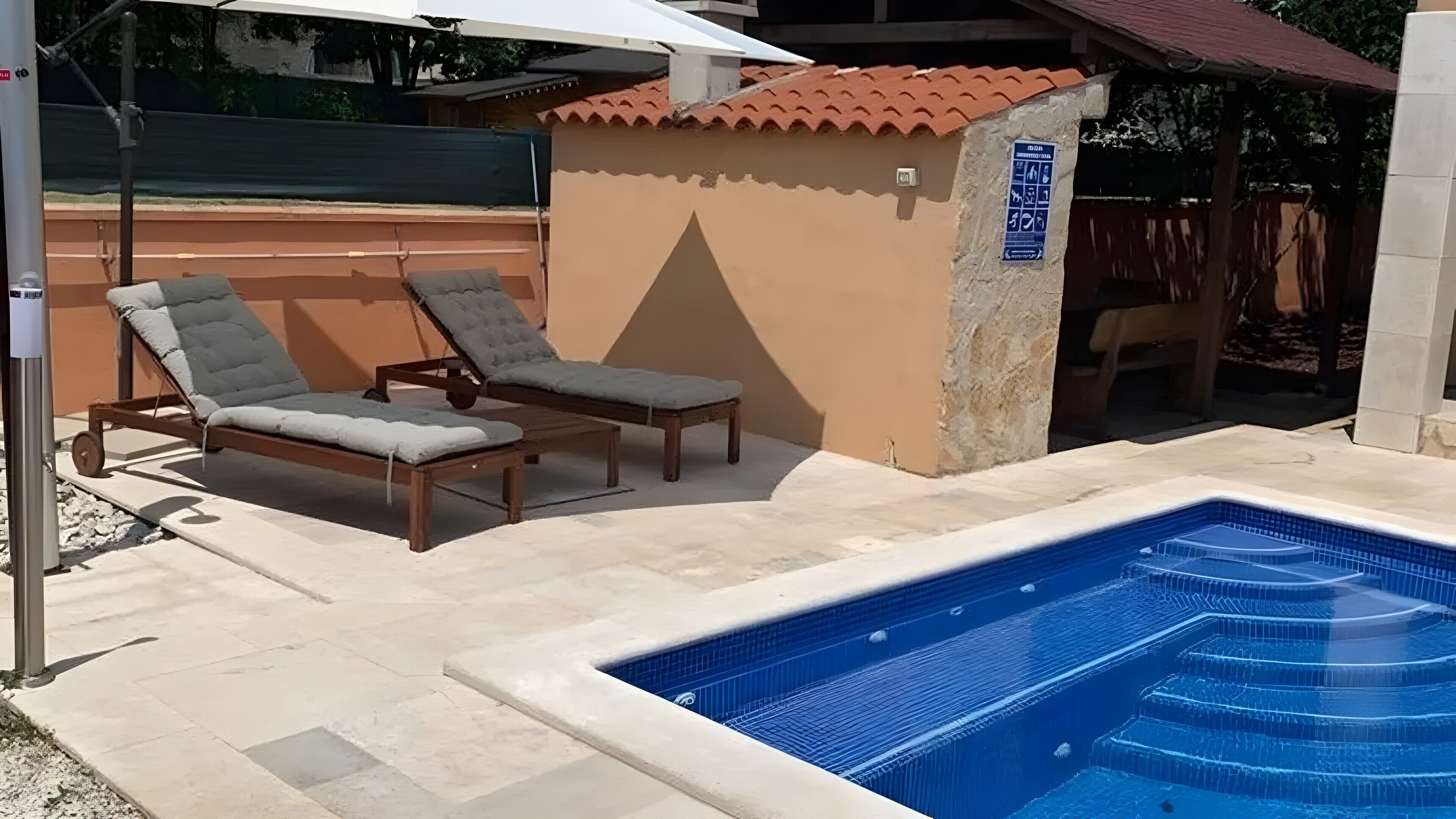 Zona de piscina con dos sillones de descanso y una pequeña construcción.