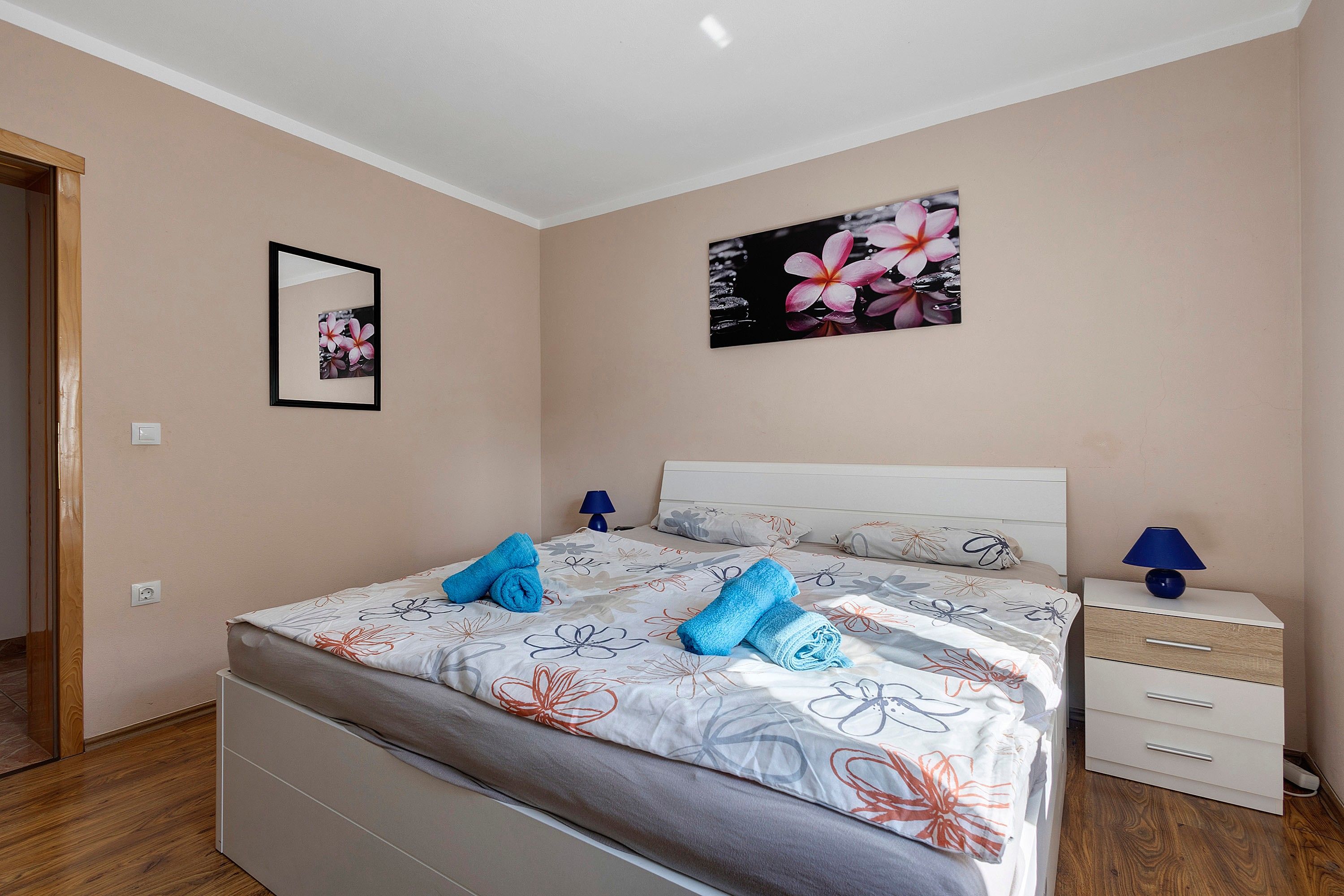 A bedroom with a bed, a nightstand, a lamp, and a wall-mounted picture.