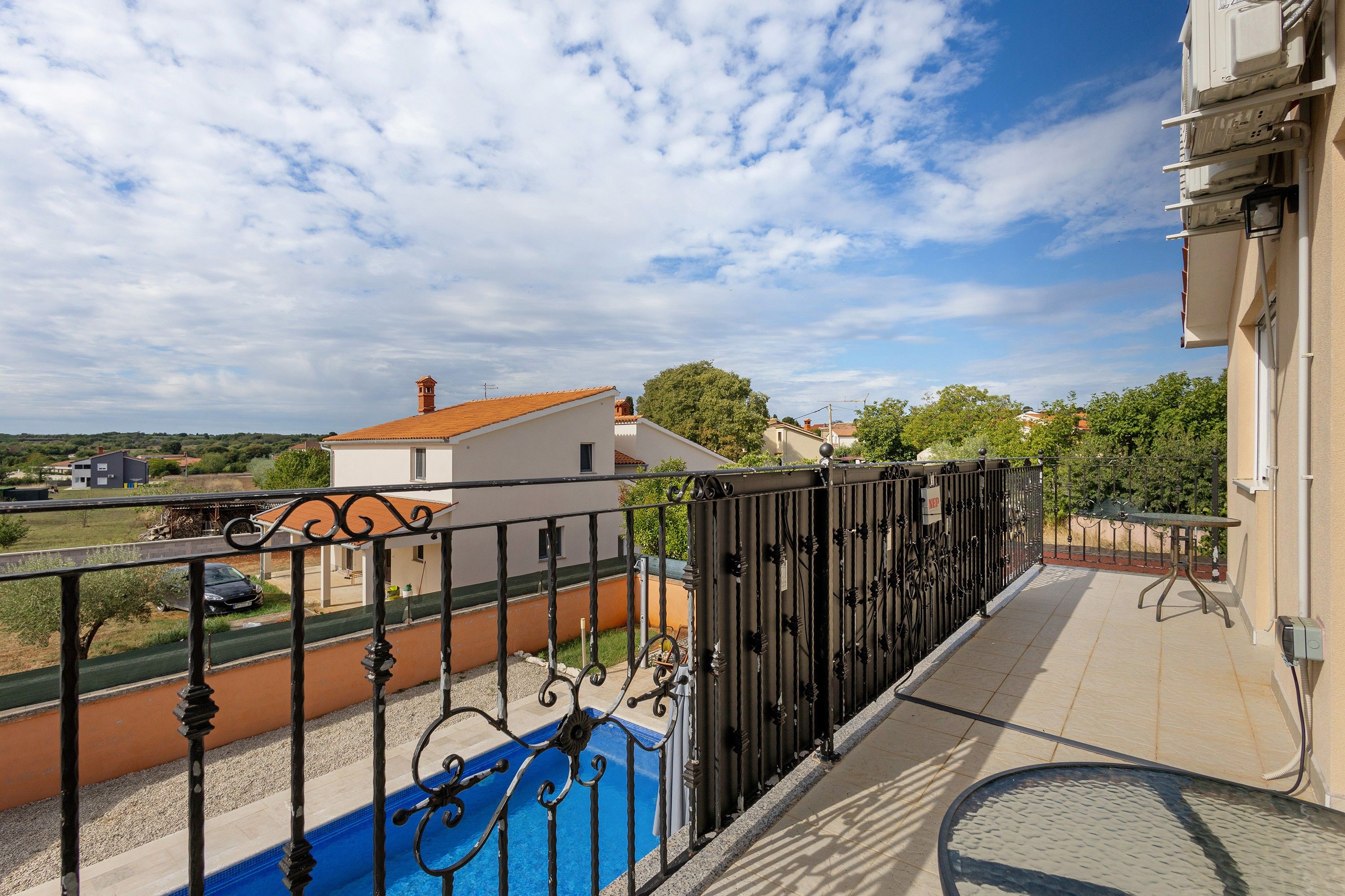 A balcony with a metal railing overlooking a swimming pool and a residential area.