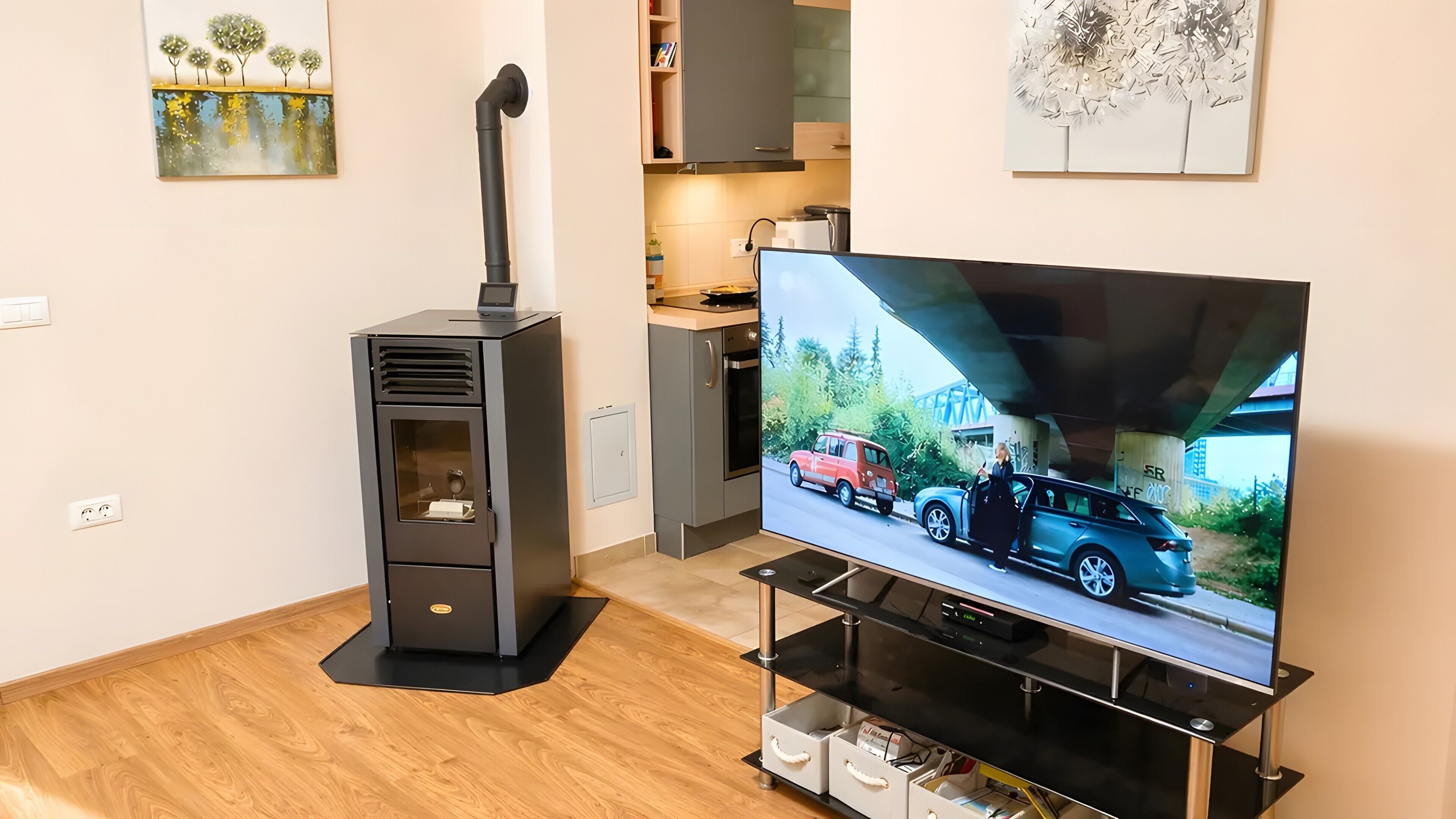 Una sala de estar moderna con un televisor de pantalla plana, un mueble de entretenimiento negro y una pequeña cocina.