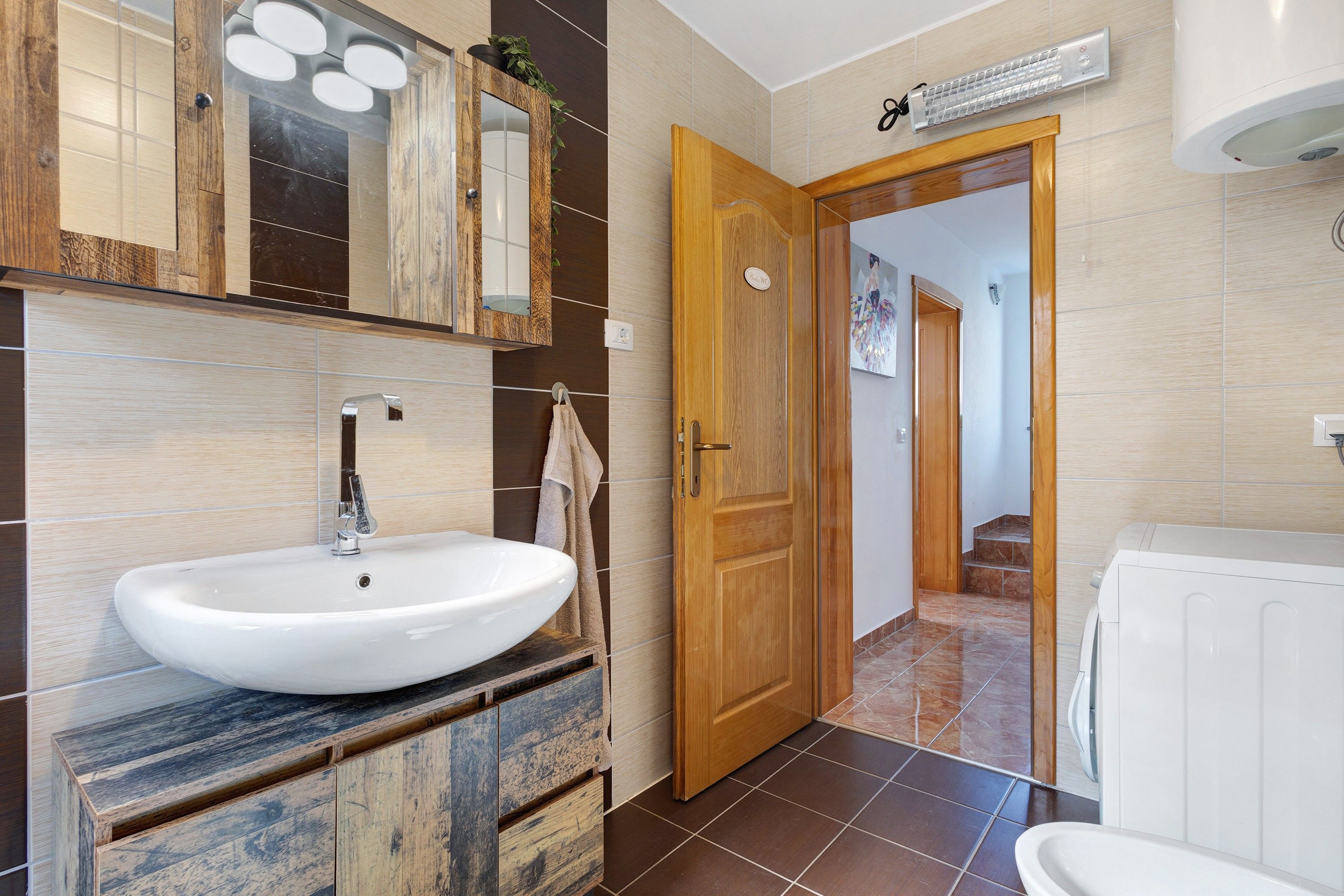 A bathroom with a white sink, wooden vanity, and a door leading to a hallway.