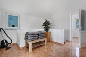 A room with a vacuum cleaner, a stack of folded blankets, a potted plant, and a window with a view.