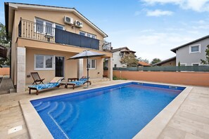A two-story building with a swimming pool, outdoor seating, and an air conditioning unit.