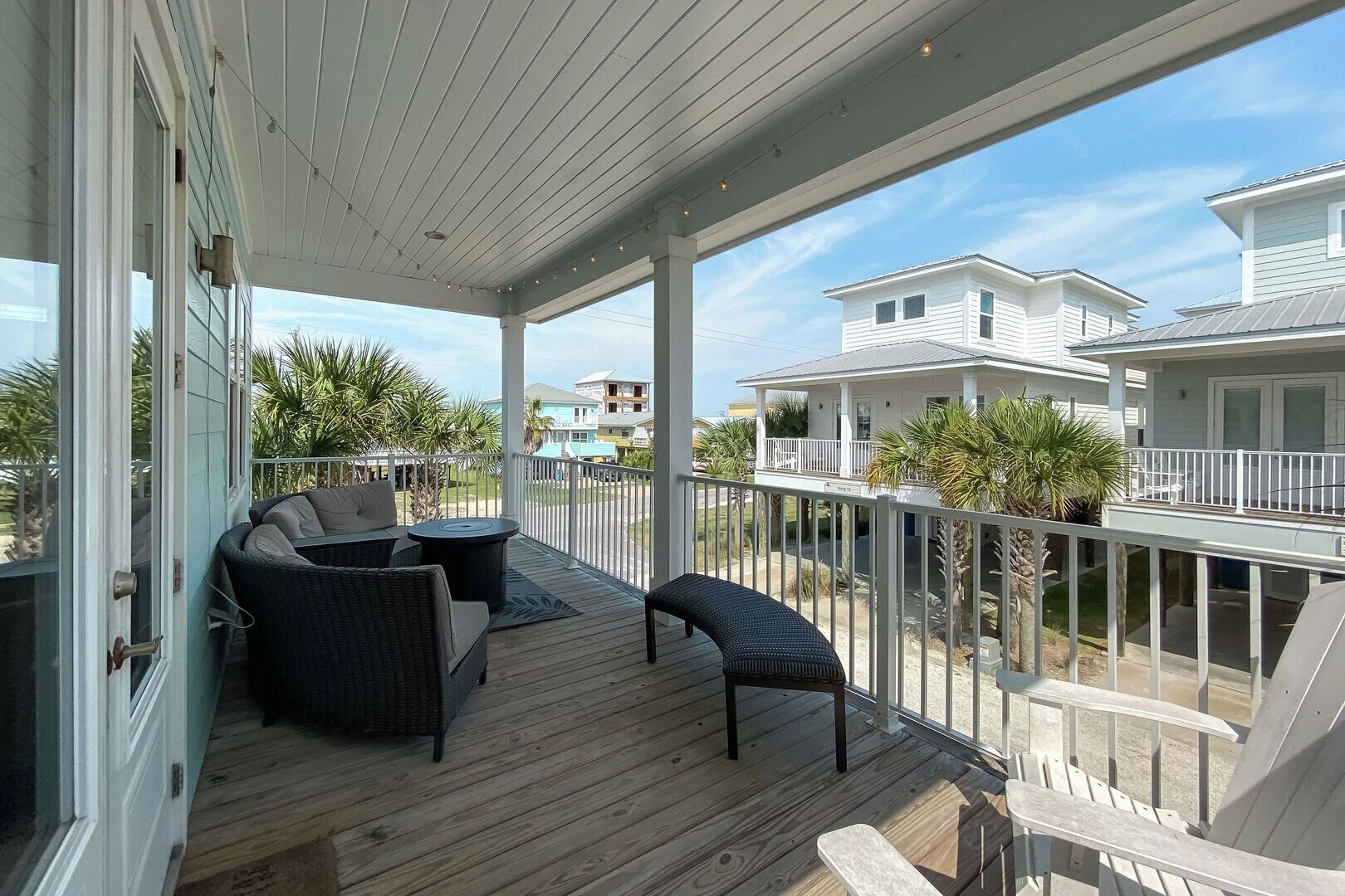 A covered outdoor deck with wicker furniture, a view of neighboring houses, and a clear sky.