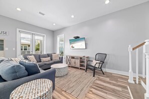 Ein geräumiges Wohnzimmer mit grauem Sofa, rundem Couchtisch und Holzboden.