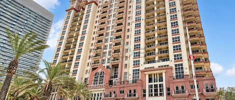 A multi-story hotel with a central entrance, balconies on each floor, and a parking area in front.