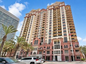 A multi-story hotel with a central entrance, balconies on each floor, and a parking area in front. - Canalfront Studio Steps from the Waterfront Promenade and Cricket Stadium (Dubai)