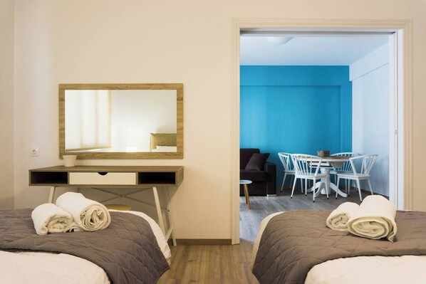 Ein Hotelzimmer mit zwei Betten, einem Schreibtisch, einem Sessel, einem kleinen Tisch und einer Essecke mit Stühlen.