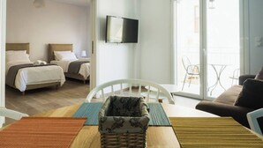 Hotellihuone, jossa on kaksi sänkyä, televisio, parveke tuoleineen sekä ruokailutila pöytineen ja tuoleineen.