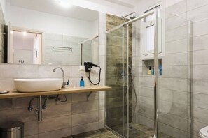 Ein modernes Badezimmer mit einer gläsernen Duschkabine, einem Waschbecken mit Spiegel darüber und einer Holzplatte.