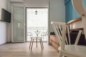 Ein Zimmer mit einer Schiebetür und einem Balkon, ein weißer Stuhl, eine Couch und ein an der Wand befestigtes Fernsehgerät.