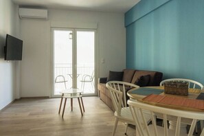 Ein Wohnzimmer mit einer Couch, einem Esstisch mit Stühlen, einem an der Wand befestigten Fernseher und einer Glastür zum Außenbereich.