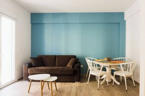 A room with a brown sofa, a white table with chairs, and a blue accent wall. - Comfort Zone Apartment in the heart of Athens (Athina)
