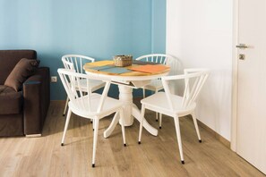 A dining area with a round table and four white chairs, a brown sofa, and a blue wall. - Comfort Zone Apartment in the heart of Athens (Athina)