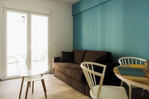 Ein Wohnzimmer mit einer Couch, einem Esstisch mit Stühlen und einer Glastür, die zu einem Außenbereich mit Sitzgelegenheiten führt.